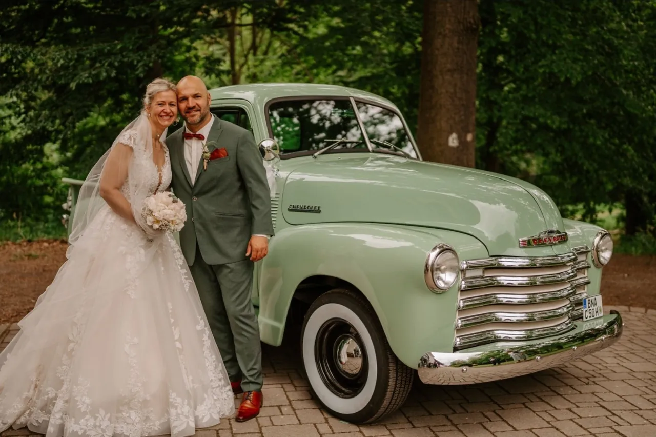 Ein Brautpaar steht lächelnd vor einem mintgrünen Oldtimer