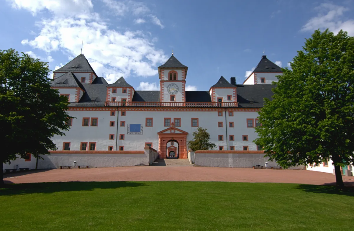 Schloss Augustusburg mit Rasenfläche und Bäumen unter blauem Himmel